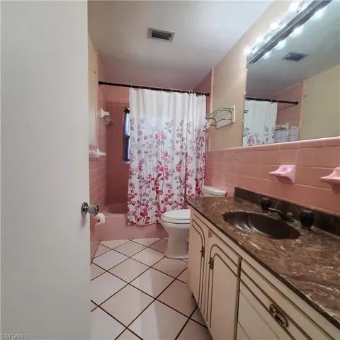 Bathroom featuring vanity, tile walls, tile patterned flooring, and shower / bath combination with curtain