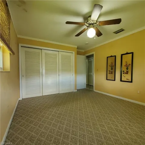 Unfurnished bedroom with a closet, carpet flooring, ornamental molding, ceiling fan, and ensuite bathroom