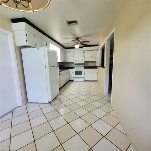 Kitchen featuring white appliances, a ceiling fan, dark countertops, white cabinetry, and light tile patterned floors