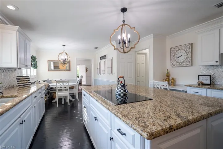 Kitchen with black electric cooktop, a notable chandelier, visible vents, and white cabinets
