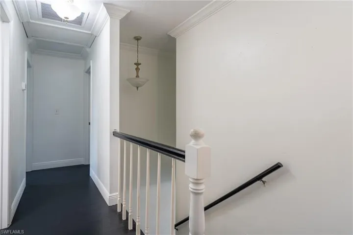 Hallway featuring wood finished floors, visible vents, baseboards, crown molding, and an upstairs landing
