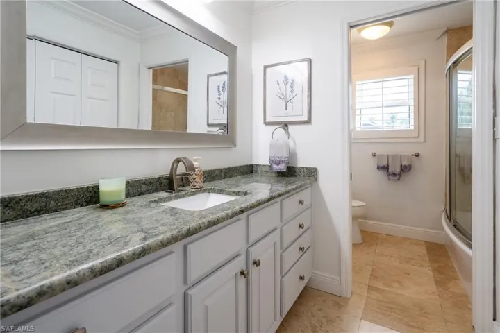 Full bathroom featuring a shower with door, toilet, vanity, and ornamental molding