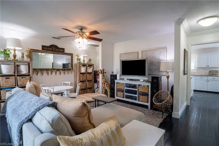 Living area with baseboards, dark wood-type flooring, ornamental molding, and a ceiling fan