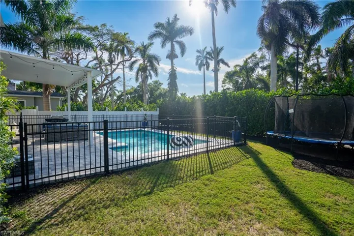 Pool with a lawn, a trampoline, and fence