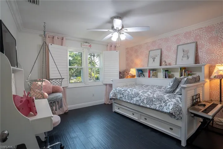 Bedroom featuring wallpapered walls, crown molding, dark wood-style floors, and baseboards