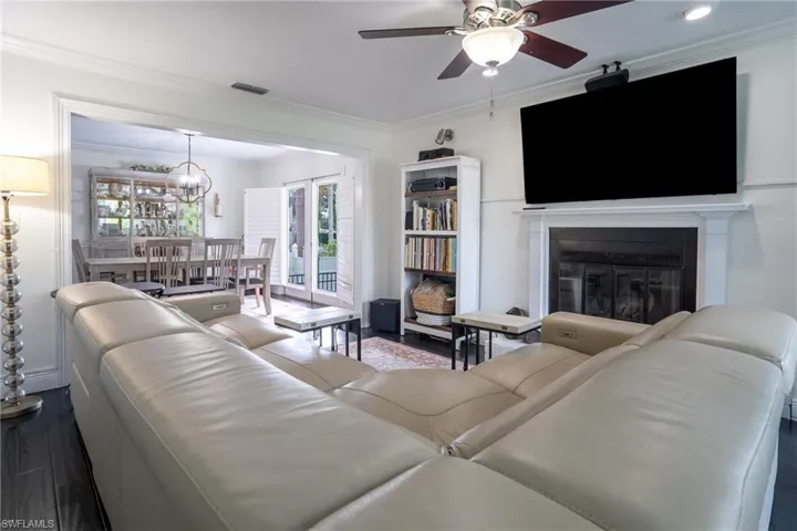 Living room with dark wood-style floors, visible vents, ornamental molding, a glass covered fireplace, and ceiling fan with notable chandelier