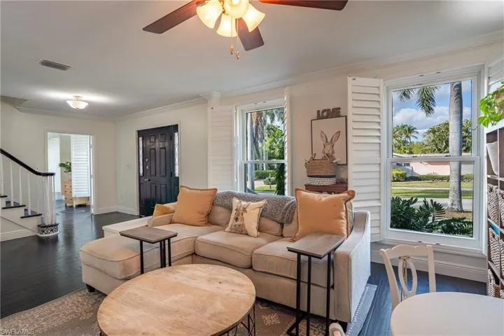 Living area featuring visible vents, dark wood-type flooring, a ceiling fan, crown molding, and stairs