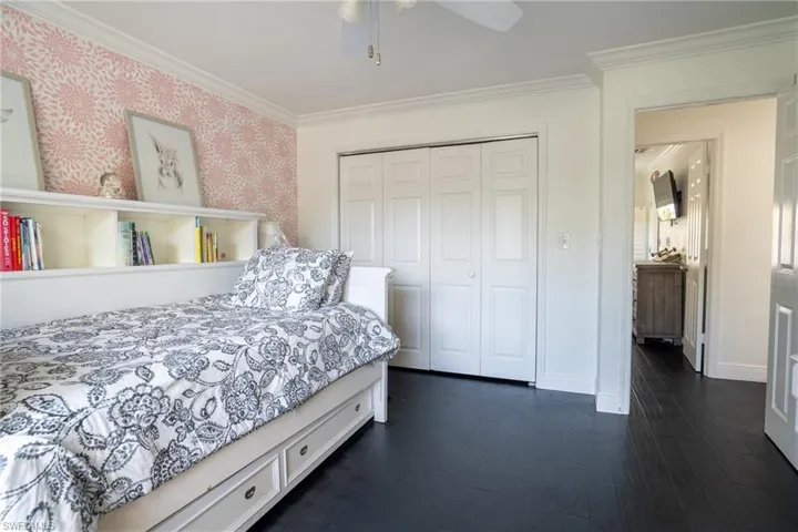 Bedroom featuring a closet, dark wood-style floors, wallpapered walls, and ornamental molding