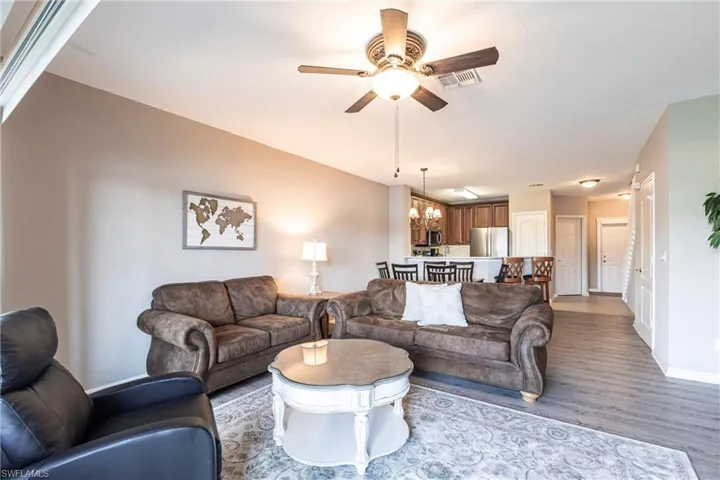Living room with ceiling fan with notable chandelier, visible vents, baseboards, and wood finished floors