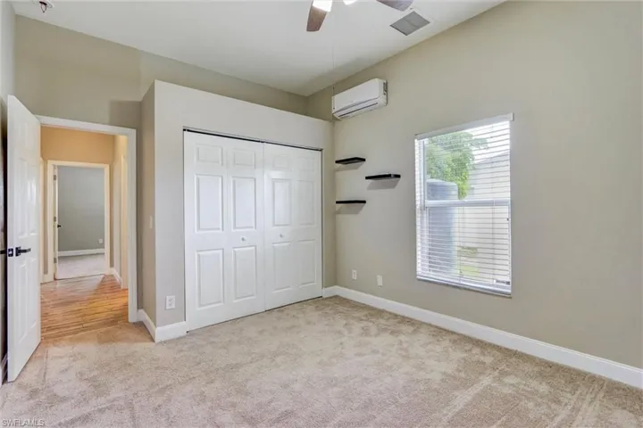 Carpeted interior space featuring a ceiling fan, a window with horizontal blinds, and a built-in split air conditioning unit