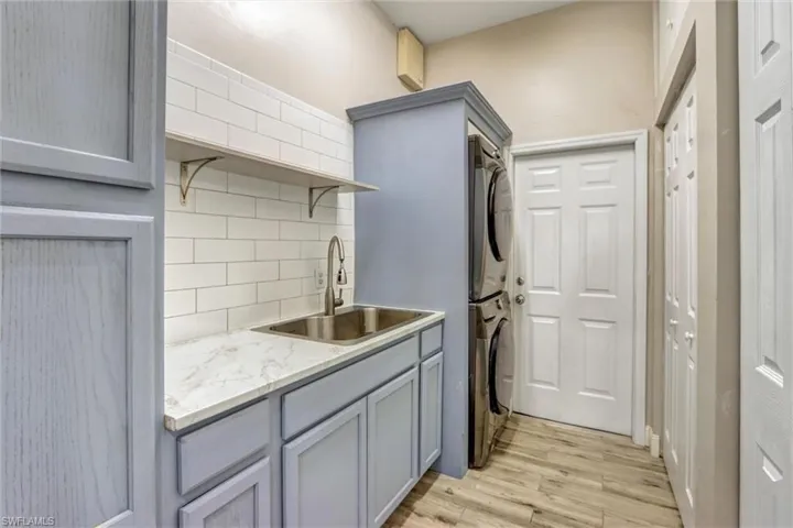 Utility room featuring light blue cabinetry, a stainless steel sink with gooseneck faucet, white subway tile backsplash, and wood-finish flooring