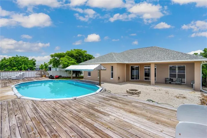 Expansive outdoor living area featuring a large above-ground swimming pool with a surrounding wood deck, a covered patio, and a fire pit area
