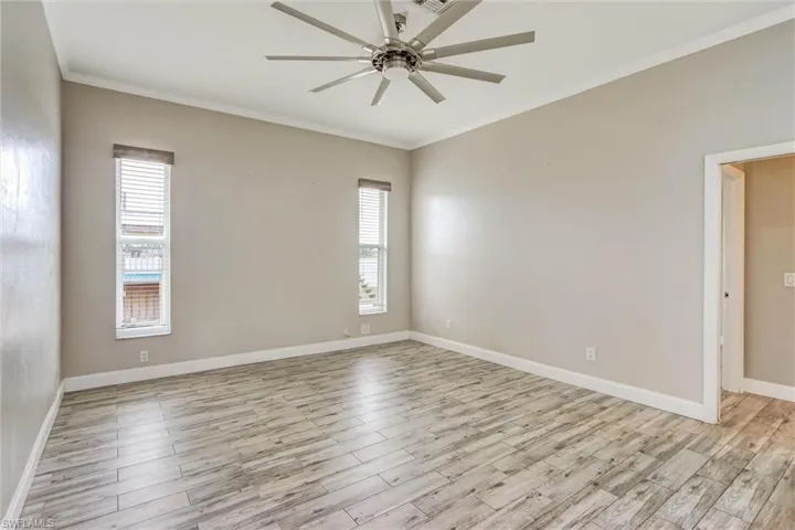 Spacious room featuring wood-finish flooring, two vertical windows with blinds, a large ceiling fan with multiple blades, and light-toned wall paint