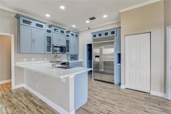 Modern kitchen featuring light blue cabinetry, stainless steel appliances, and a central island with a sink and breakfast bar