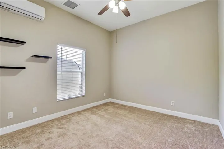 Carpeted interior space featuring a window with blinds, ceiling fan, and wall-mounted air conditioning unit