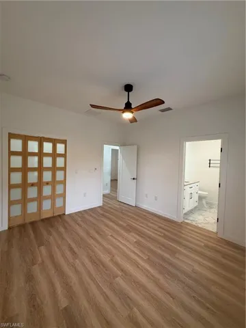 Unfurnished bedroom with ceiling fan, ensuite bathroom, and light wood-style flooring