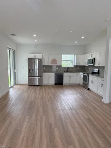 Kitchen with decorative backsplash, white cabinetry, refrigerator, and stove