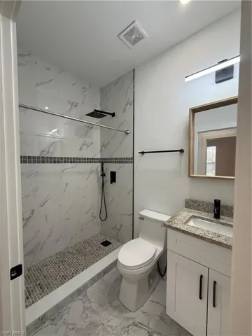 Full bathroom with vanity, a marble finish shower, and light marble finish flooring