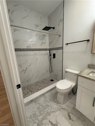 Full bath with vanity, a marble finish shower, a textured wall, and light marble finish flooring