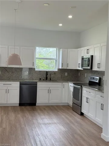 Kitchen with range, white cabinetry, light stone counters, decorative backsplash, and light wood-style floors