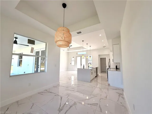 Unfurnished dining area featuring a tray ceiling, recessed lighting, and light marble finish floors