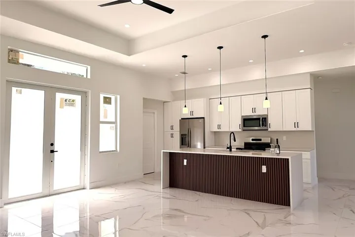 Kitchen with white cabinets, a kitchen island with sink, stainless steel appliances, a high ceiling, and light marble finish flooring