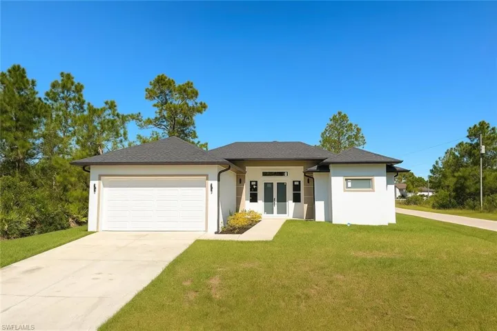 Prairie-style home featuring french doors, a front lawn, an attached garage, driveway, and stucco siding
