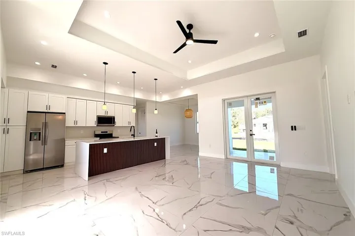 Kitchen featuring open floor plan, stainless steel appliances, french doors, white cabinetry, and a kitchen island with sink