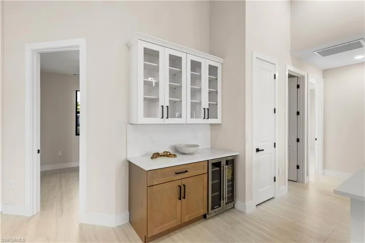 Built-in BUTLER'S PANTRY w/ quartz countertop, glass-front cabinetry, warm wood base cabinets & WINE REFRIGERATOR, ideal for BEVERAGE STATION, COFFEE BAR, or EXTRA STORAGE & PREP SPACE. GLASS-FRONT UPPER CABINETS add touch of ELEGANCE & DISPLAY STORAGE!