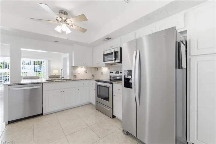 Kitchen with stainless steel appliances, white cabinets, a tray ceiling, light stone countertops, and a ceiling fan