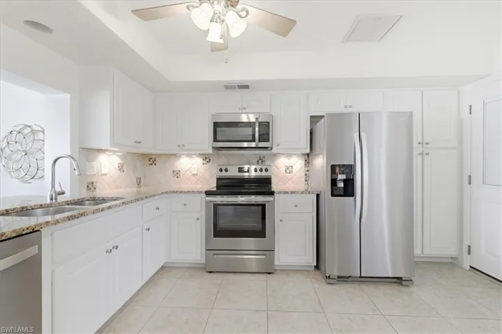 Kitchen with stainless steel appliances, light stone counters, white cabinetry, ceiling fan, and a raised ceiling