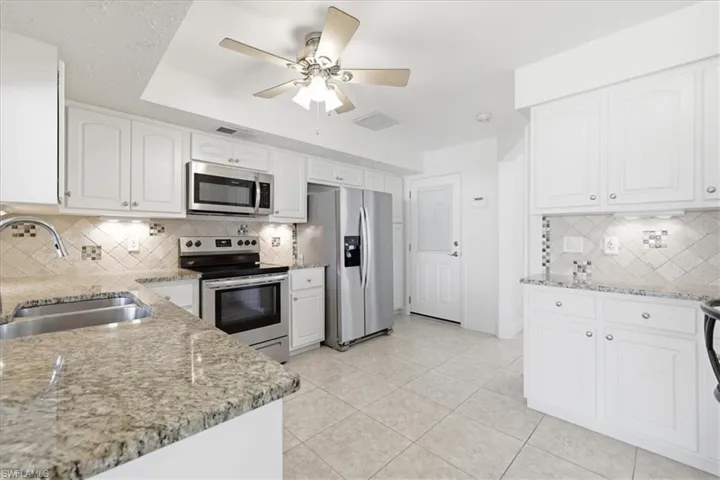 Kitchen featuring stainless steel appliances, light stone countertops, white cabinetry, and ceiling fan