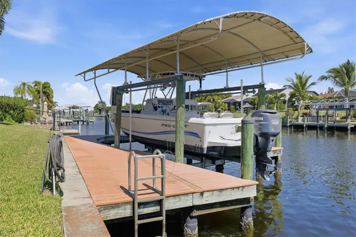 Dock with a water view, boat lift, and a lawn