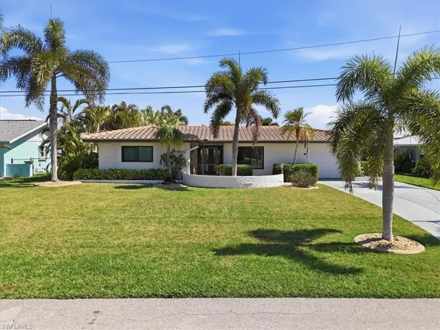Ranch-style home with concrete driveway, an attached garage, a front lawn, a tiled roof, and stucco siding