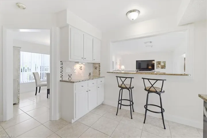Kitchen with a breakfast bar, white cabinets, light stone counters, tasteful backsplash, and light tile patterned floors