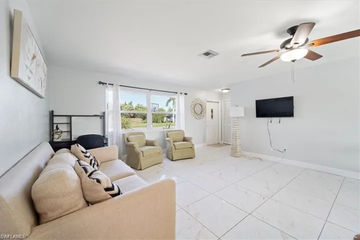 Living room featuring a ceiling fan, light marble finish flooring, and baseboards