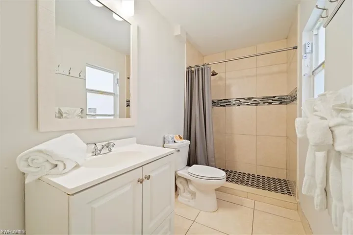 Full bathroom with tiled shower, toilet, vanity, and tile patterned floors