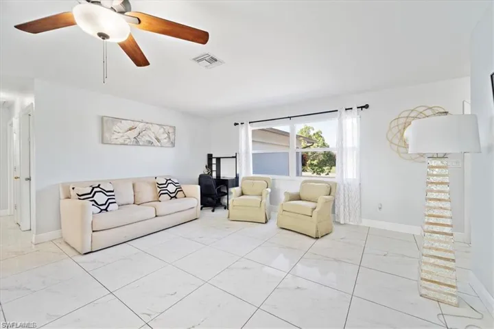 Living room featuring light marble finish flooring, ceiling fan, and baseboards
