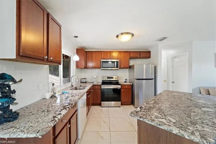 Kitchen with appliances with stainless steel finishes, a sink, brown cabinets, and light stone countertops