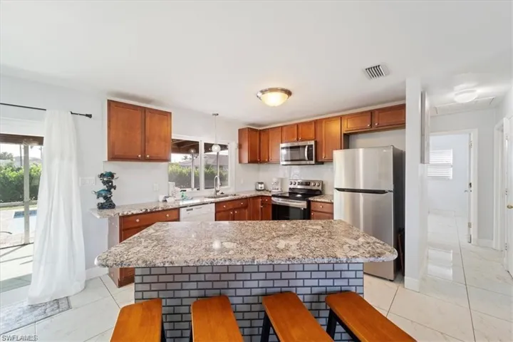 Kitchen featuring appliances with stainless steel finishes, a sink, brown cabinetry, and healthy amount of natural light