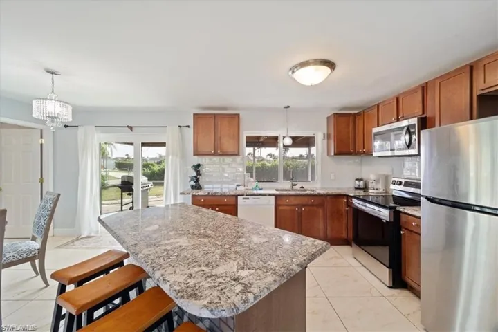Kitchen featuring appliances with stainless steel finishes, a sink, brown cabinets, a chandelier, and a kitchen island
