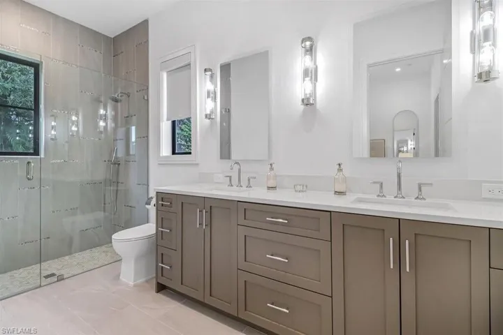 Bathroom featuring toilet, a shower with shower door, vanity, and a wealth of natural light