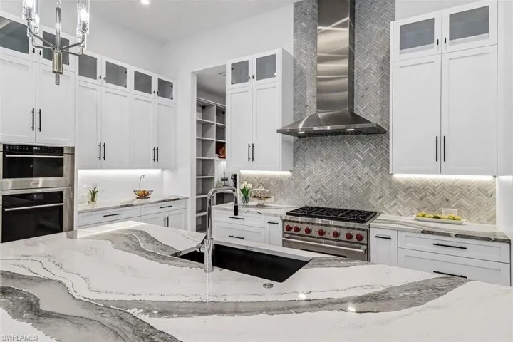 Kitchen featuring wall chimney range hood, stainless steel appliances, light stone counters, and pendant lighting