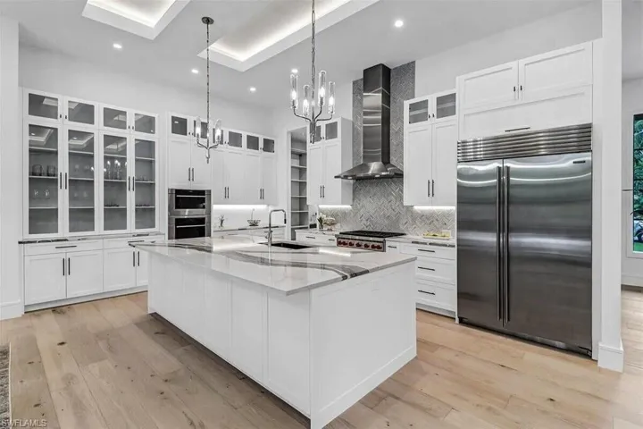 Kitchen featuring wall chimney range hood, an island with sink, appliances with stainless steel finishes, light hardwood / wood-style floors, and sink