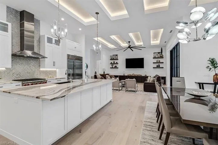 Kitchen featuring wall chimney exhaust hood, a large island with sink, appliances with stainless steel finishes, and white cabinets
