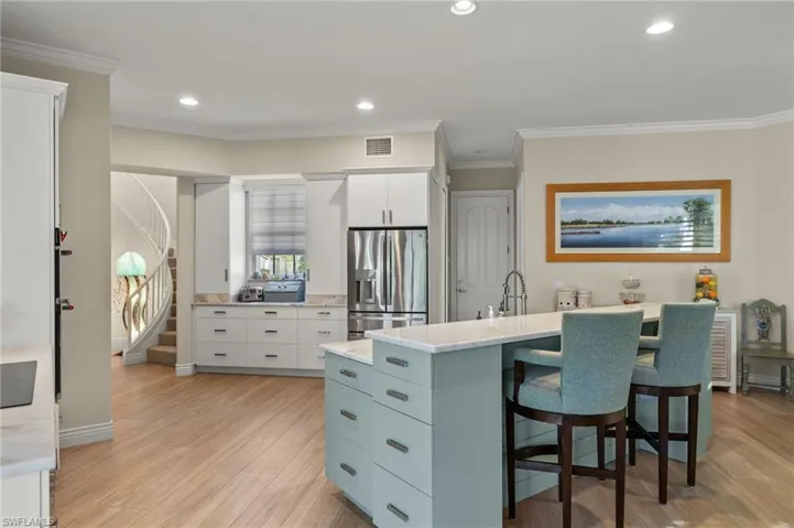 Kitchen with ornamental molding, light wood-type flooring, white cabinetry, and stainless steel fridge