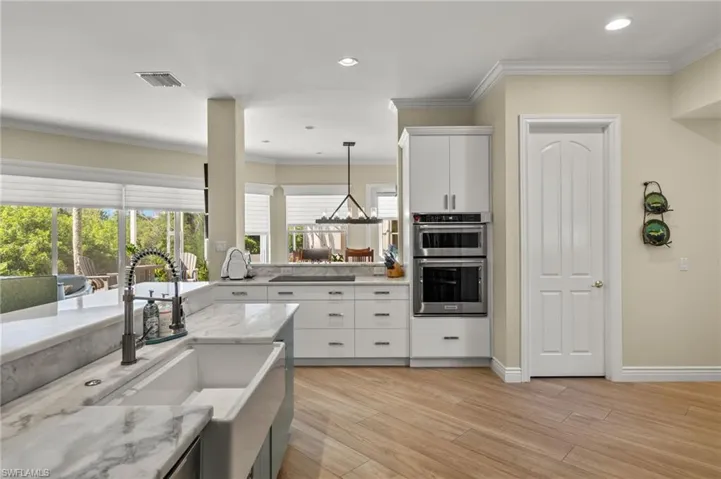 Kitchen featuring pendant lighting, light stone counters, white cabinets, light hardwood / wood-style flooring, and double oven
