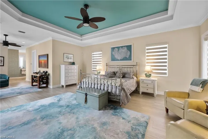 Bedroom with ceiling fan, ornamental molding, light wood-type flooring, and a raised ceiling