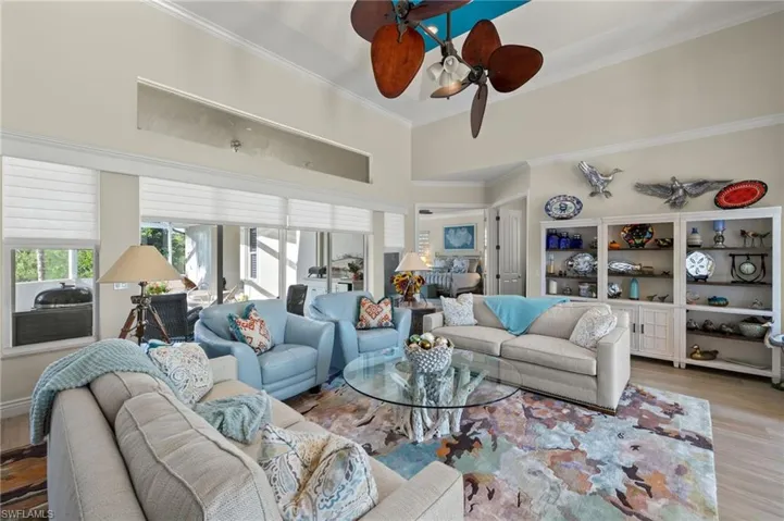 Living room featuring ceiling fan, light wood-type flooring, ornamental molding, and a high ceiling