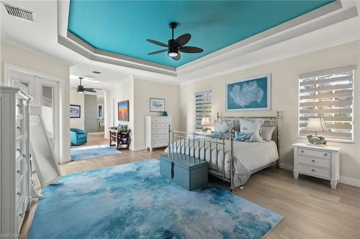 Bedroom featuring ceiling fan, ornamental molding, light hardwood / wood-style flooring, and a tray ceiling